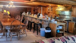 A rustic log cabin interior with a dining area, kitchen, and a large painting of a snowy scene. - Beautiful Lodge for Weddings, Reunions, Events or Family Gatherings. Sleeps 25+ (Redfield)