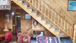 A wooden staircase leading to an upper level, a black leather sofa with a large teddy bear, and a dining area with red chairs. - Beautiful Lodge for Weddings, Reunions, Events or Family Gatherings. Sleeps 25+ (Redfield)