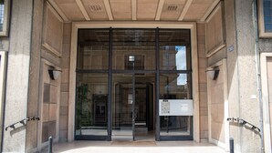 Une entrée d’immeuble dotée d’une porte en verre, d’une grille de sécurité en métal et d’un boîtier d’alarme incendie.