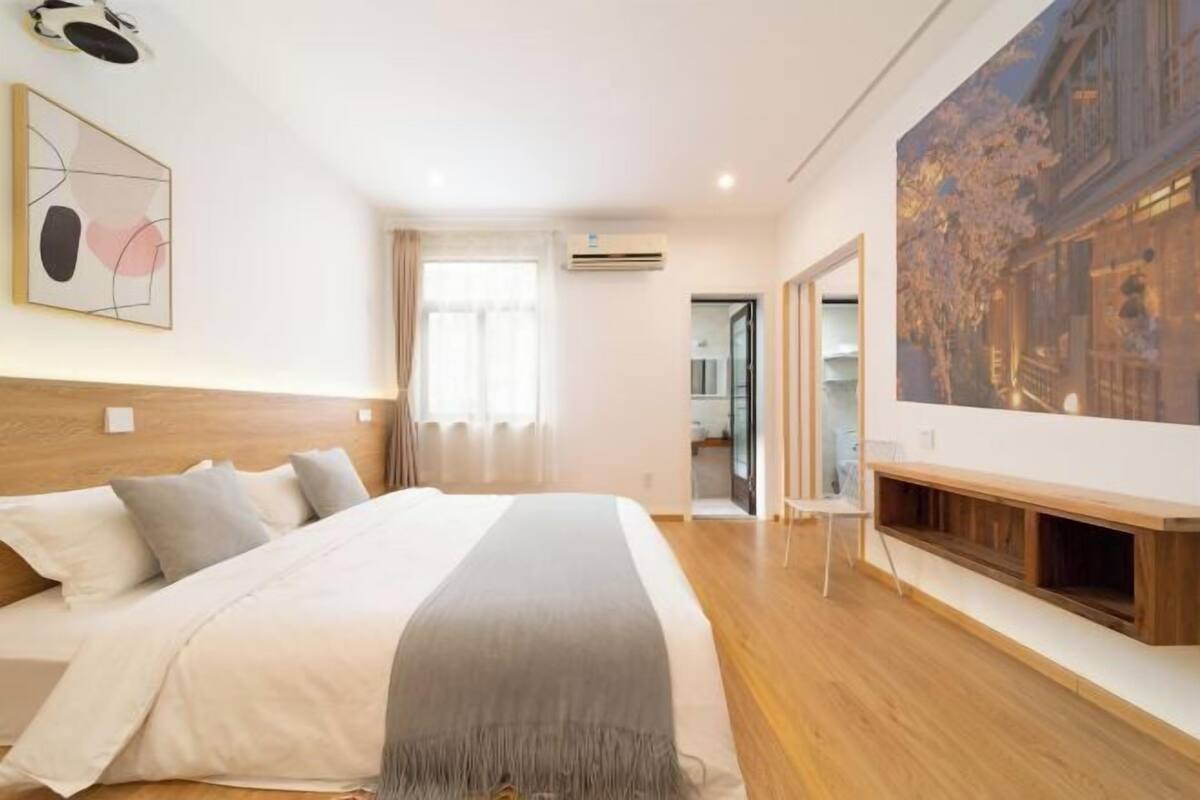 A modern bedroom with a large bed, a wooden headboard, a bedside table, and a large window with curtains.