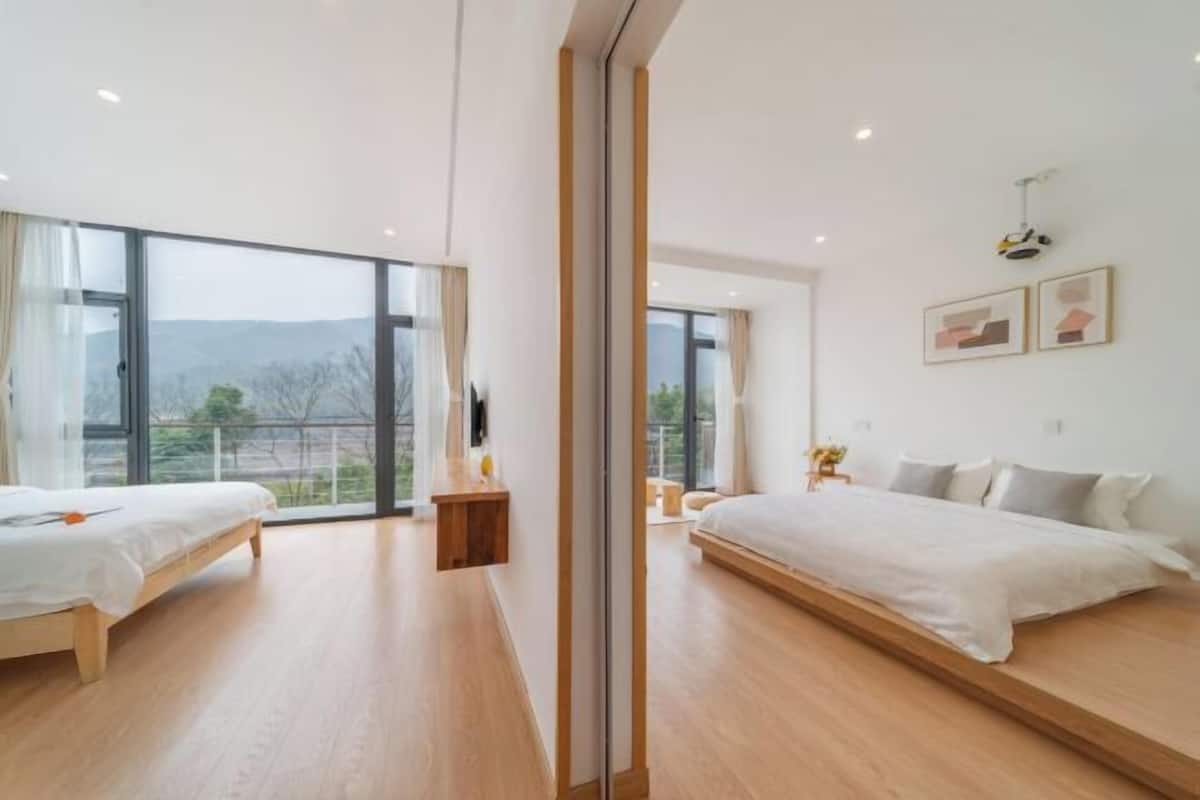 A modern bedroom with two beds, large windows, and a view of the outdoors.