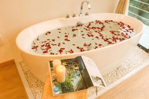 A bathtub filled with water and rose petals, a candle, and an open magazine on a wooden tray. - Yuanshan Hostel (Deqing)