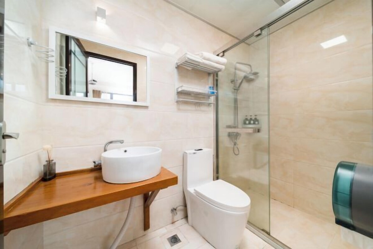 A modern bathroom with a wooden vanity, a white sink, a toilet, and a glass shower enclosure.
