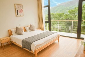 A bedroom with a large bed, a nightstand, a bedside table, and a view of a balcony with a railing. - Yuanshan Hostel (Deqing)