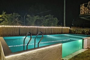 A rectangular swimming pool with metal ladders, surrounded by a stone wall and a bamboo fence. - Yuanshan Hostel (Deqing)