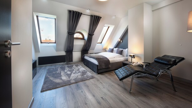 A modern bedroom with a bed, a reclining chair, a window with curtains, and a skylight. - Small Venice Apartments (Wroclaw)