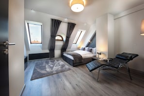 Ein modernes Schlafzimmer mit einem Bett, einem Liegestuhl, einem Fenster mit Vorhängen und einem Dachfenster.