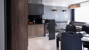 A modern kitchen with dark wood cabinets, a black countertop, and a dining area with a table and chairs. - Small Venice Apartments (Wroclaw)