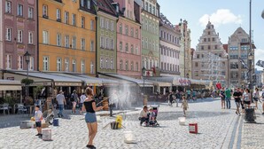 A cobblestone square with colorful historic buildings, outdoor seating, and a fountain. - Small Venice Apartments (Wroclaw)