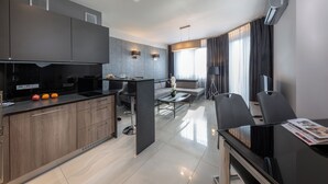 A modern kitchen with dark cabinetry, a central island, and a dining area with a glass table and chairs. - Small Venice Apartments (Wroclaw)
