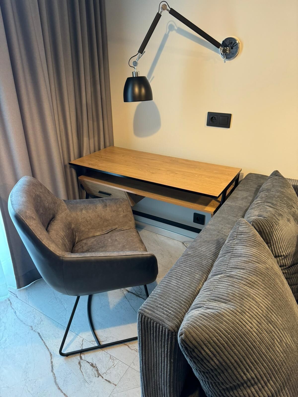 A modern living room with a wooden desk, a black armchair, and a grey sofa.