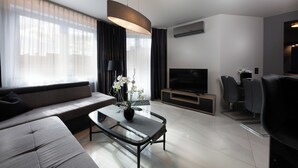 A modern living room with a sofa, a glass coffee table with a vase of flowers, a flat-screen TV, and a dining area with chairs. - Small Venice Apartments (Wroclaw)
