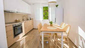 A modern kitchen with wooden cabinets, a built-in oven, and a dining area with a table and chairs. - Apartment Riva Parenzo (Porec)
