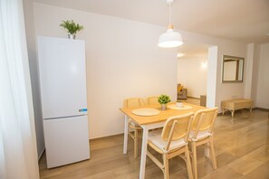 A modern kitchen with a white refrigerator, wooden dining table, wicker chairs, and a hanging light fixture.