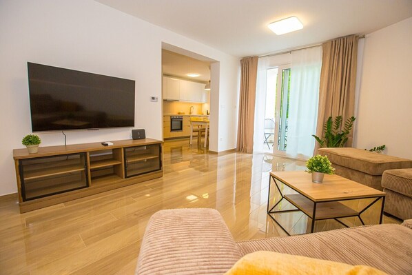 Un salon moderne doté d’un téléviseur à écran plat, d’un meuble de rangement en bois et d’un coin repas avec une cuisine en arrière-plan.