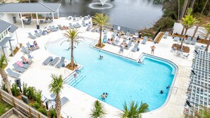 Une piscine entourée de chaises longues et de palmiers, le tout bordé d’une terrasse couverte.