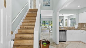 Une cuisine moderne avec des meubles blancs, un lave-vaisselle en acier inoxydable et un escalier en bois.