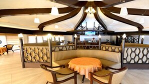 Ein Restaurant mit einer zentralen Sitzgruppe, die aus einem runden Tisch und Stühlen besteht, einer hohen Decke mit markanter Architektur und einer Bar im Hintergrund.