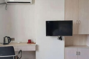 A room with a flat-screen TV mounted on the wall, a desk with a kettle, and a chair. - Xiangzhi Hotel (Yueqing)