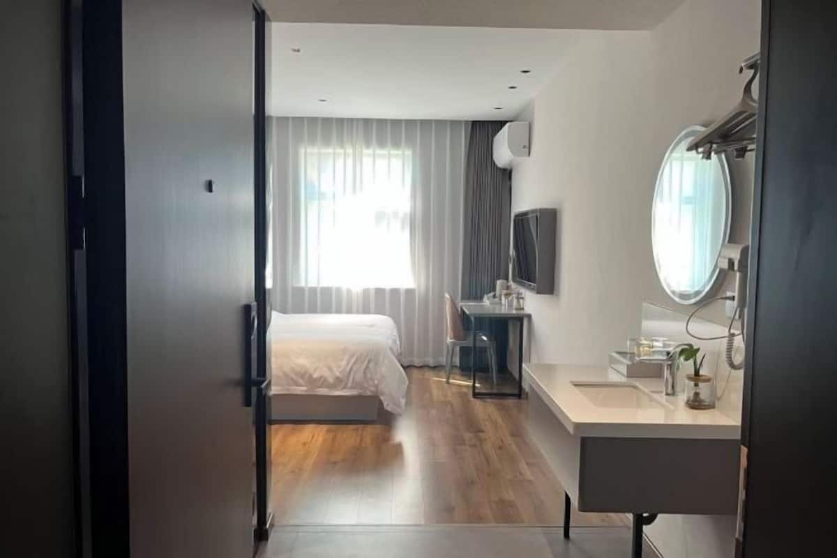 Ein Hotelzimmer mit Bett, Schreibtisch, Spiegel und einem Fenster mit Vorhängen.