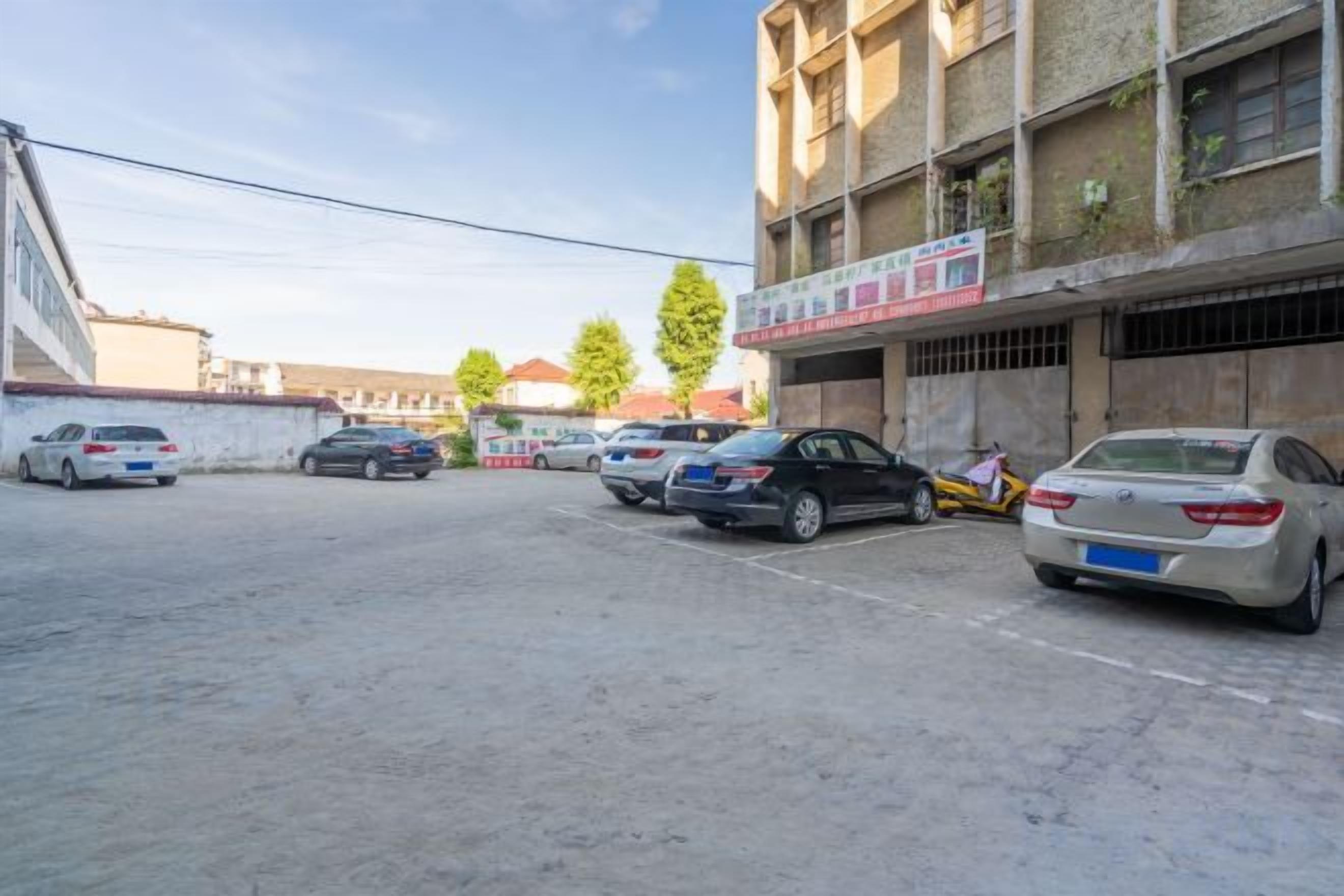 A parking lot with several cars, a building with multiple floors and balconies, and a clear sky.