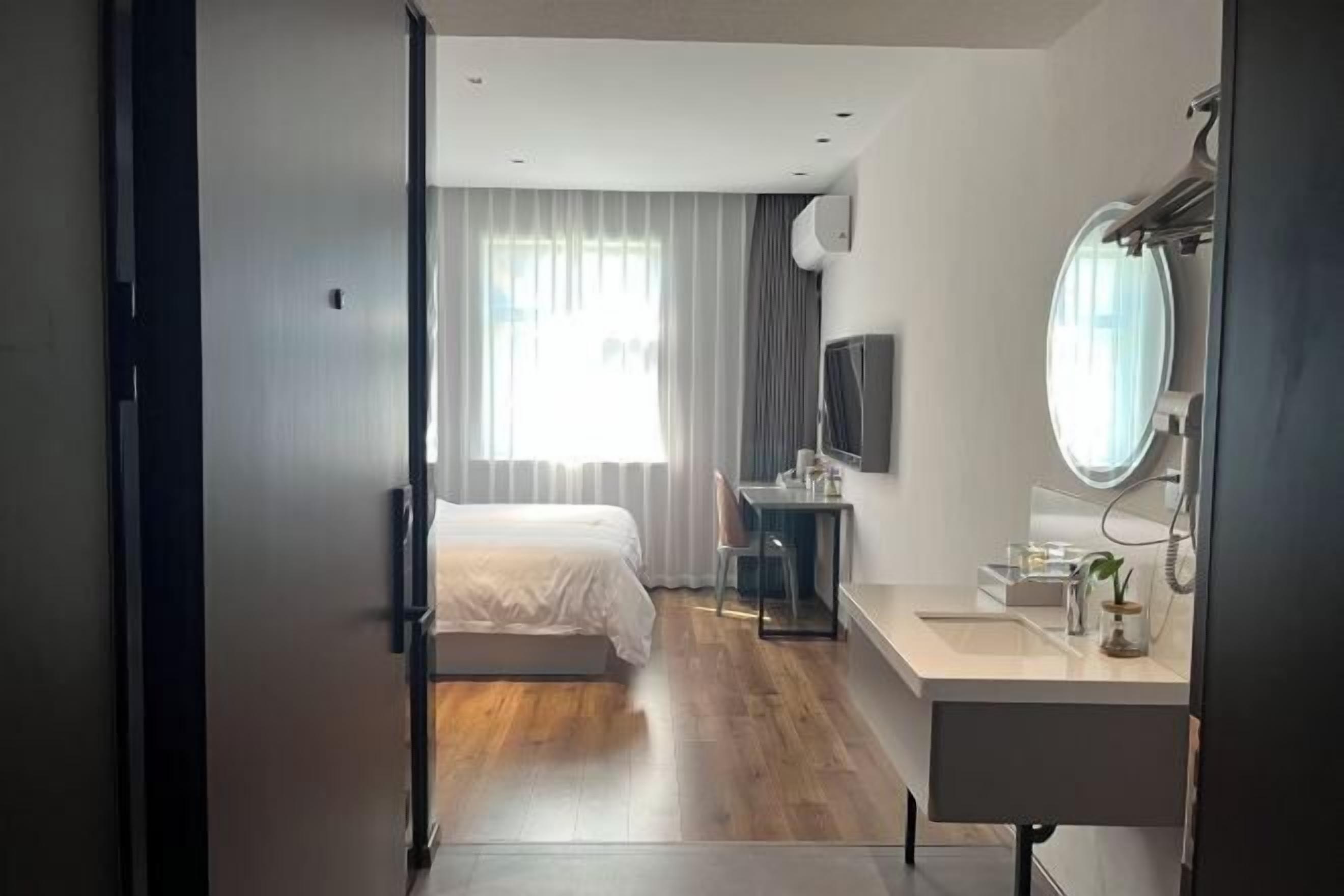 Una habitación de hotel moderna con cama, escritorio, silla, televisor y baño con espejo.