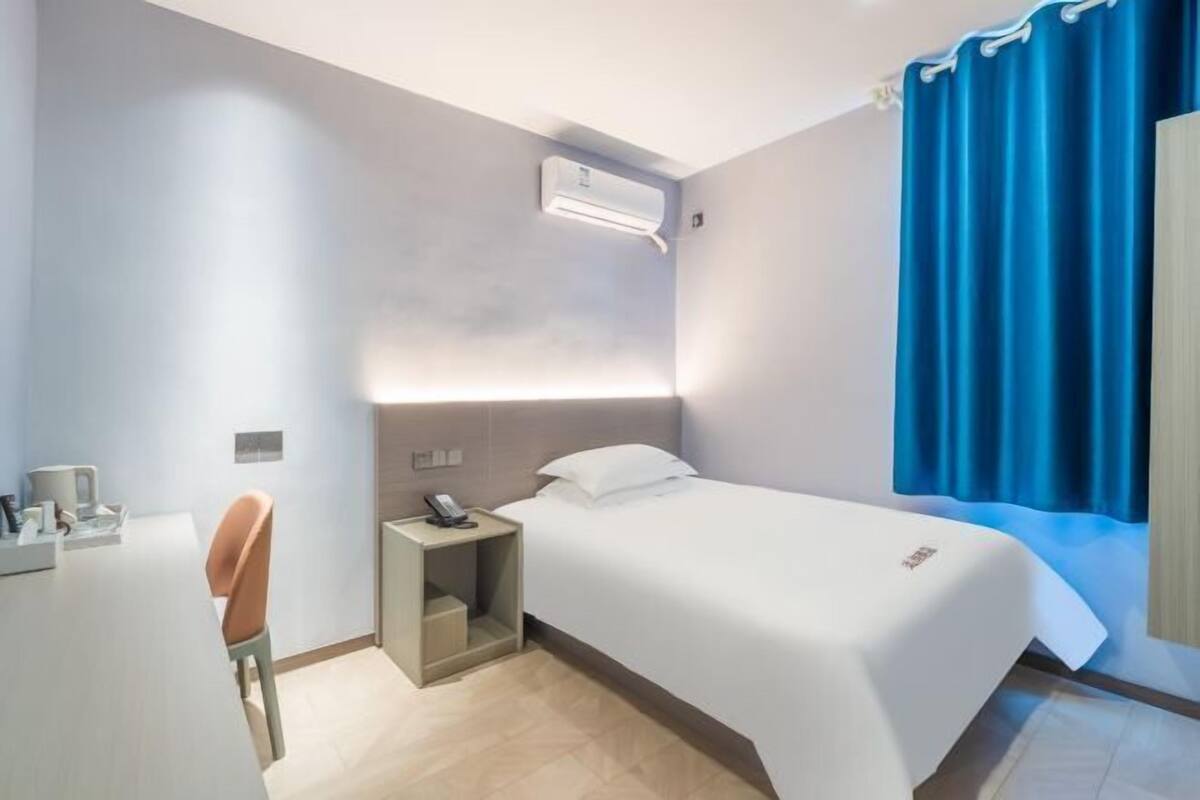 Ein Hotelzimmer mit Bett, Nachttisch, Stuhl, Schreibtisch und Klimaanlage.