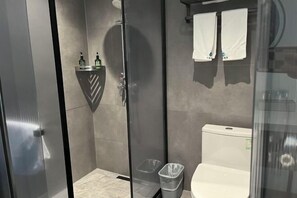 Uma casa de banho moderna com chuveiro em cabine de vidro, sanita e um cesto de lixo.