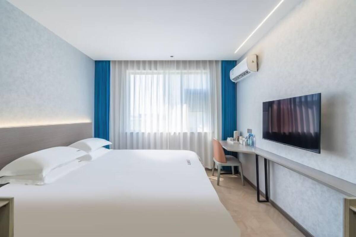 Ein Hotelzimmer mit Bett, Schreibtisch, Stuhl, Fernseher und einem Vorhangfenster.