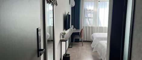 Habitación de hotel con cama, escritorio, silla, una mesita con planta, espejo y ventana con cortinas.