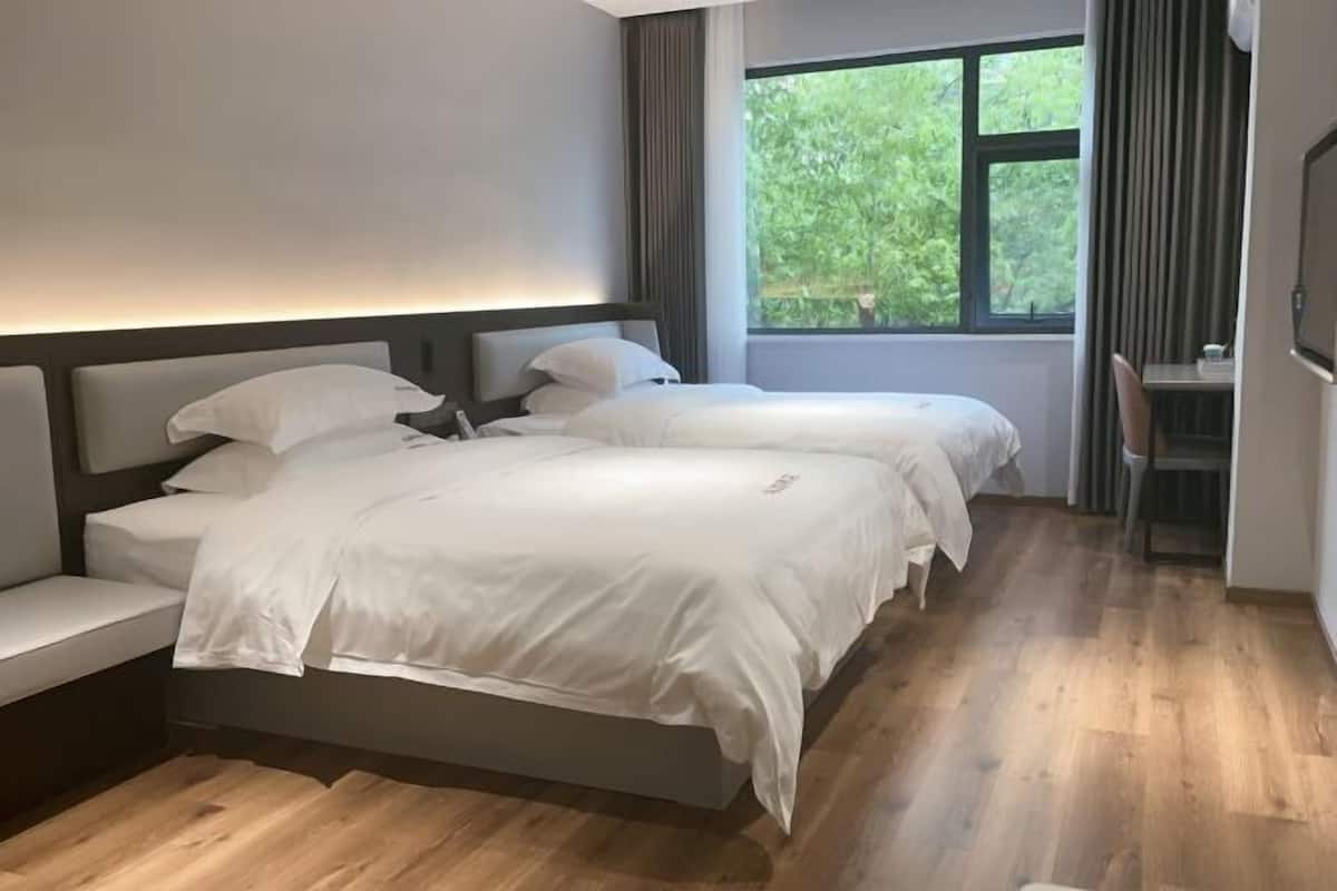 Ein Schlafzimmer mit zwei Betten, einem Schreibtisch und einem Fenster mit Blick auf Grünflächen.