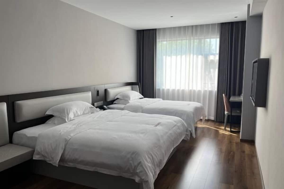 Ein modernes Hotelzimmer mit zwei Betten, einem Flachbildfernseher und einem großen Fenster mit Vorhängen.