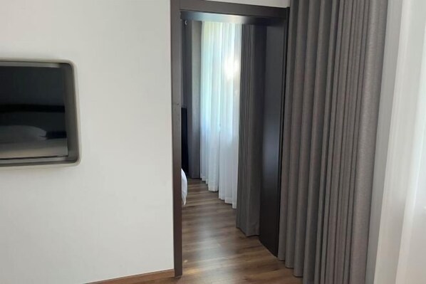 Um corredor estreito com piso de madeira e cortinas cinzentas em ambos os lados.