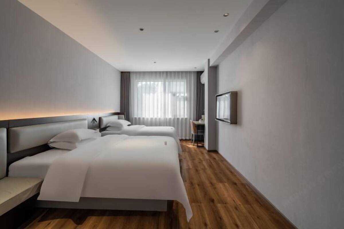 Ein modernes Hotelzimmer mit einem großen Bett, Nachttischen, einem Schreibtisch und einem Fenster mit Vorhängen.