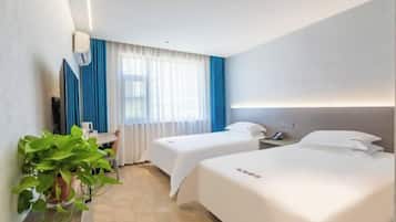 Habitación de hotel con dos camas, un escritorio, una silla, una planta en maceta y una ventana con cortinas.