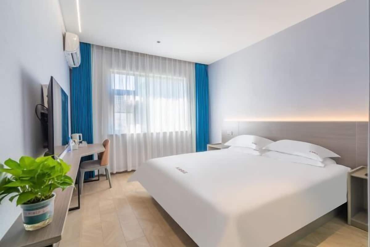 Ein Hotelzimmer mit einem großen Bett, einem Schreibtisch mit Stuhl, einem Fernseher und einer Pflanze.