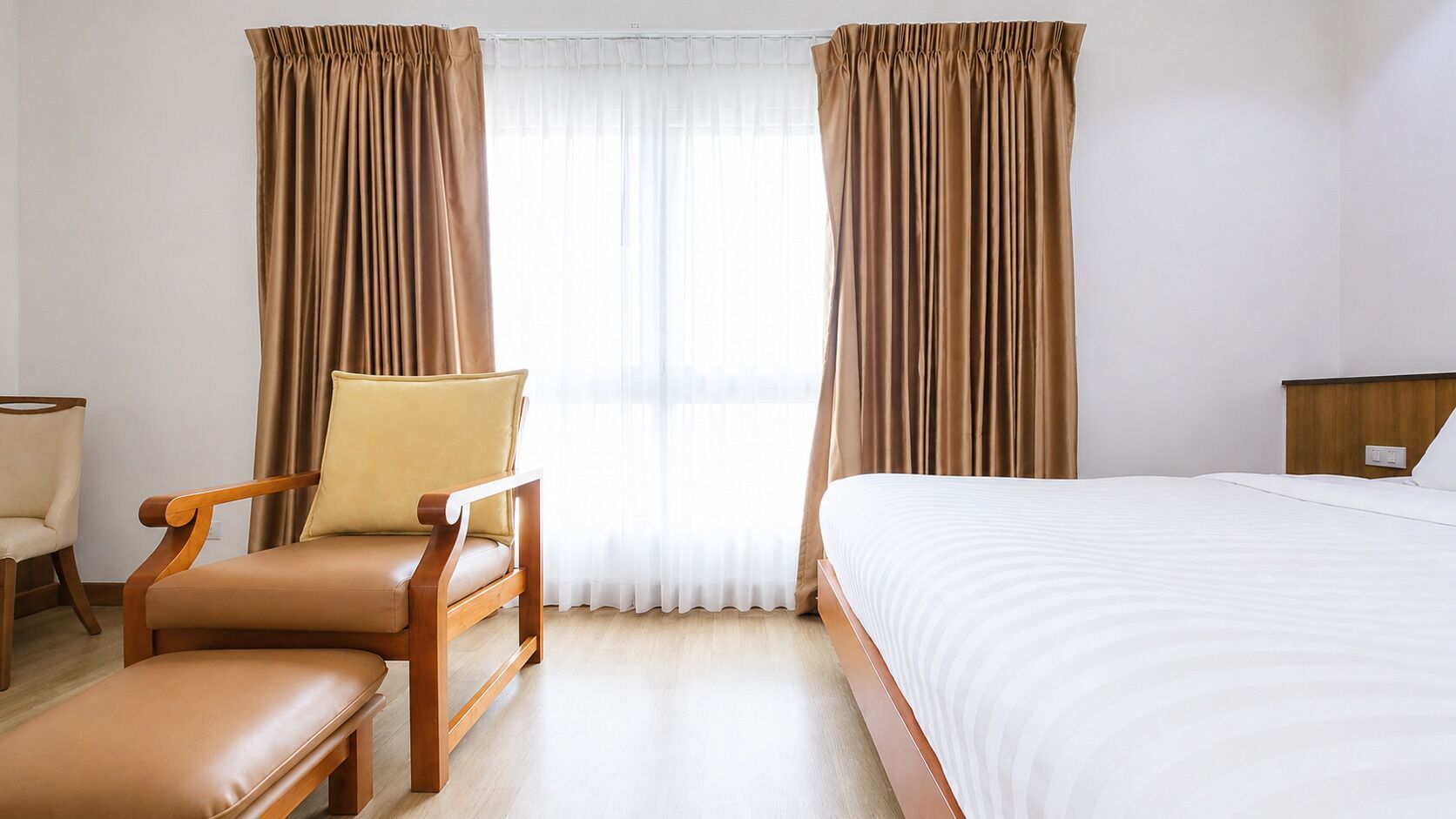 A hotel room with a bed, a chair, a bench, and curtains.