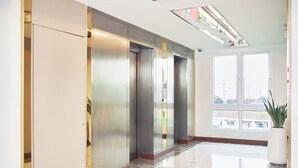 A modern elevator area with a marble floor and a large window offering a city view. - Cozy Don Mueang Hotel (Bangkok)