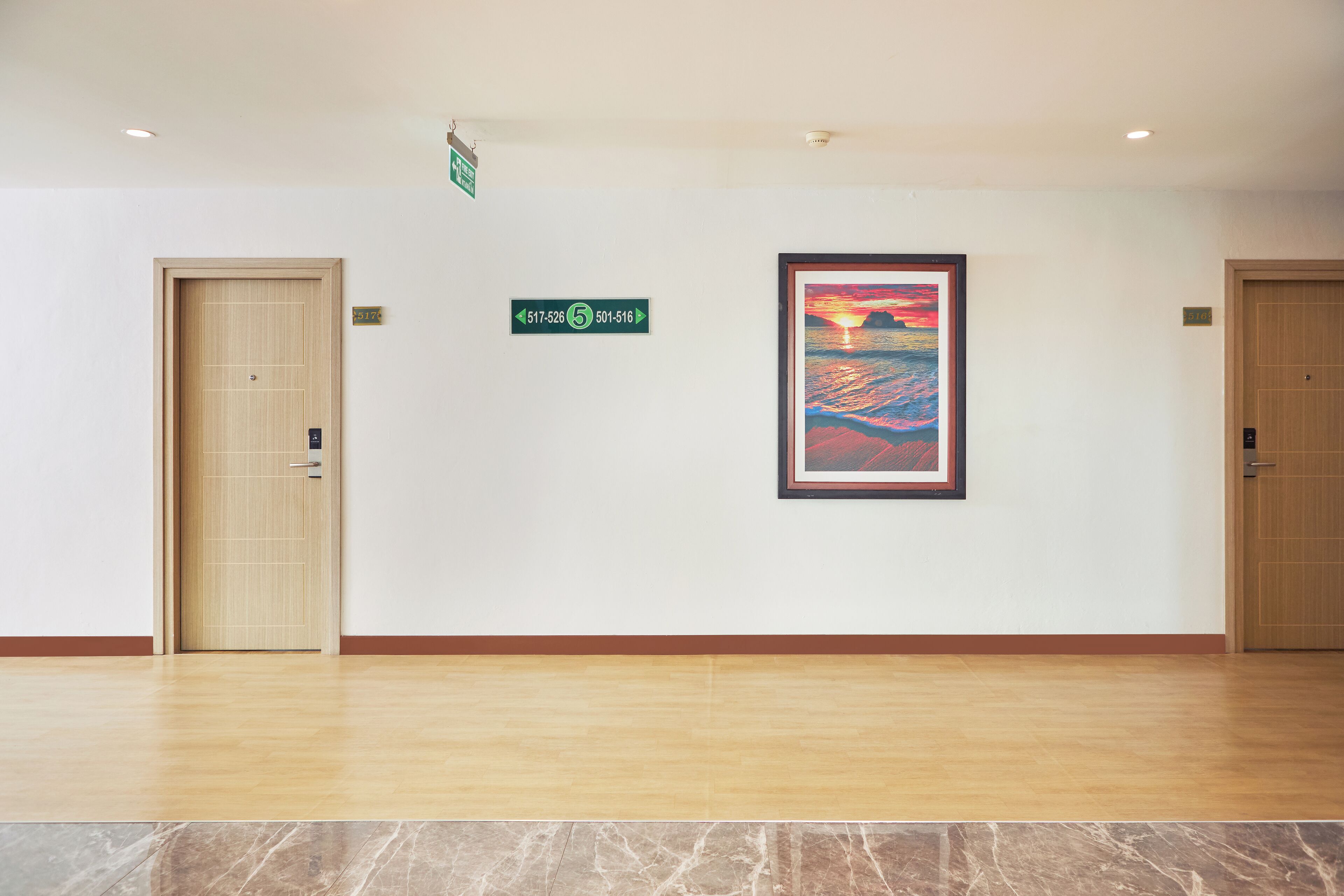 Un vestíbulo de hotel con suelo de madera, dos puertas de madera, un cuadro enmarcado de un atardecer y señales direccionales.
