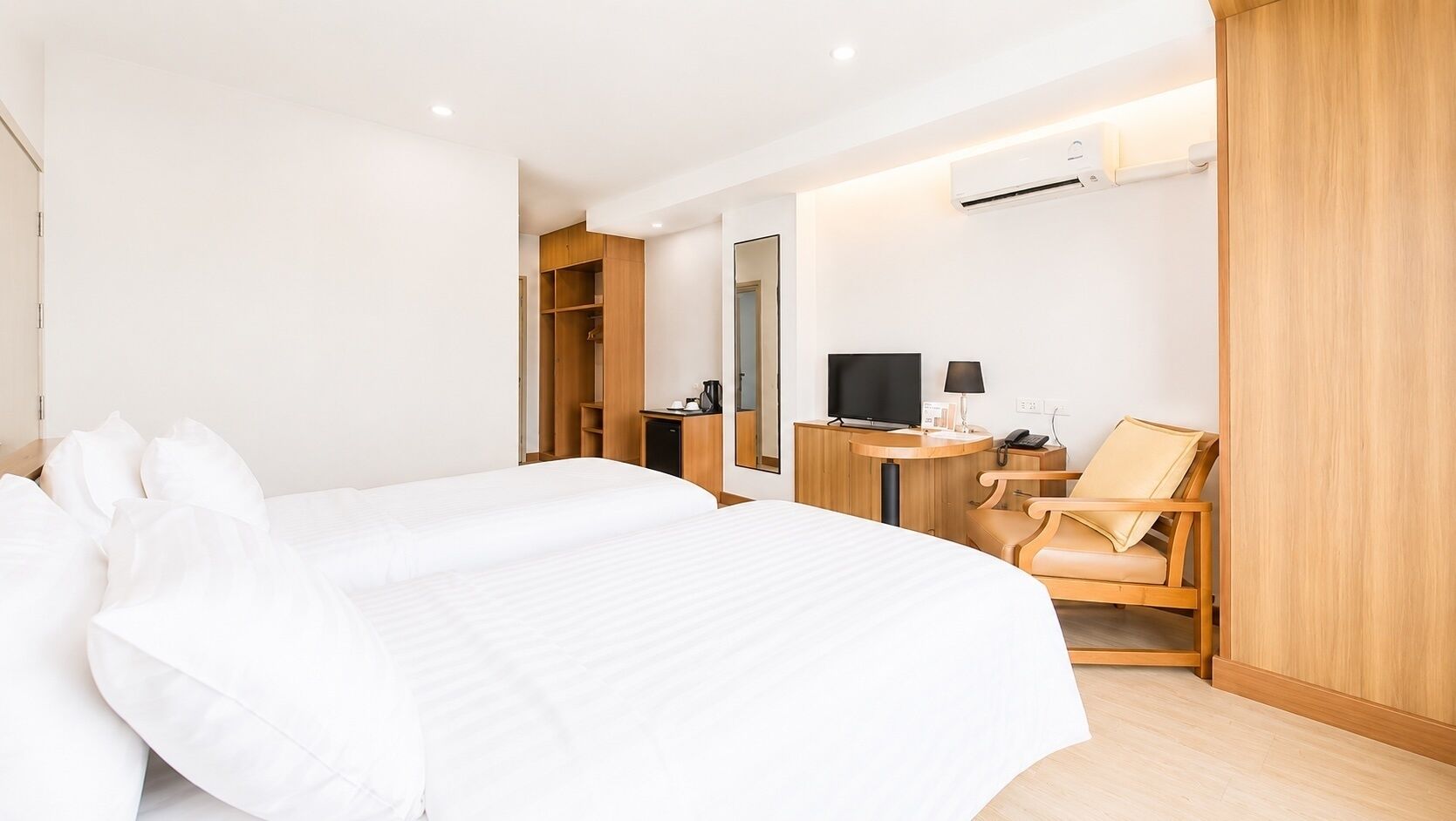 A hotel room with two beds, a desk with a TV, a chair, and a wardrobe.