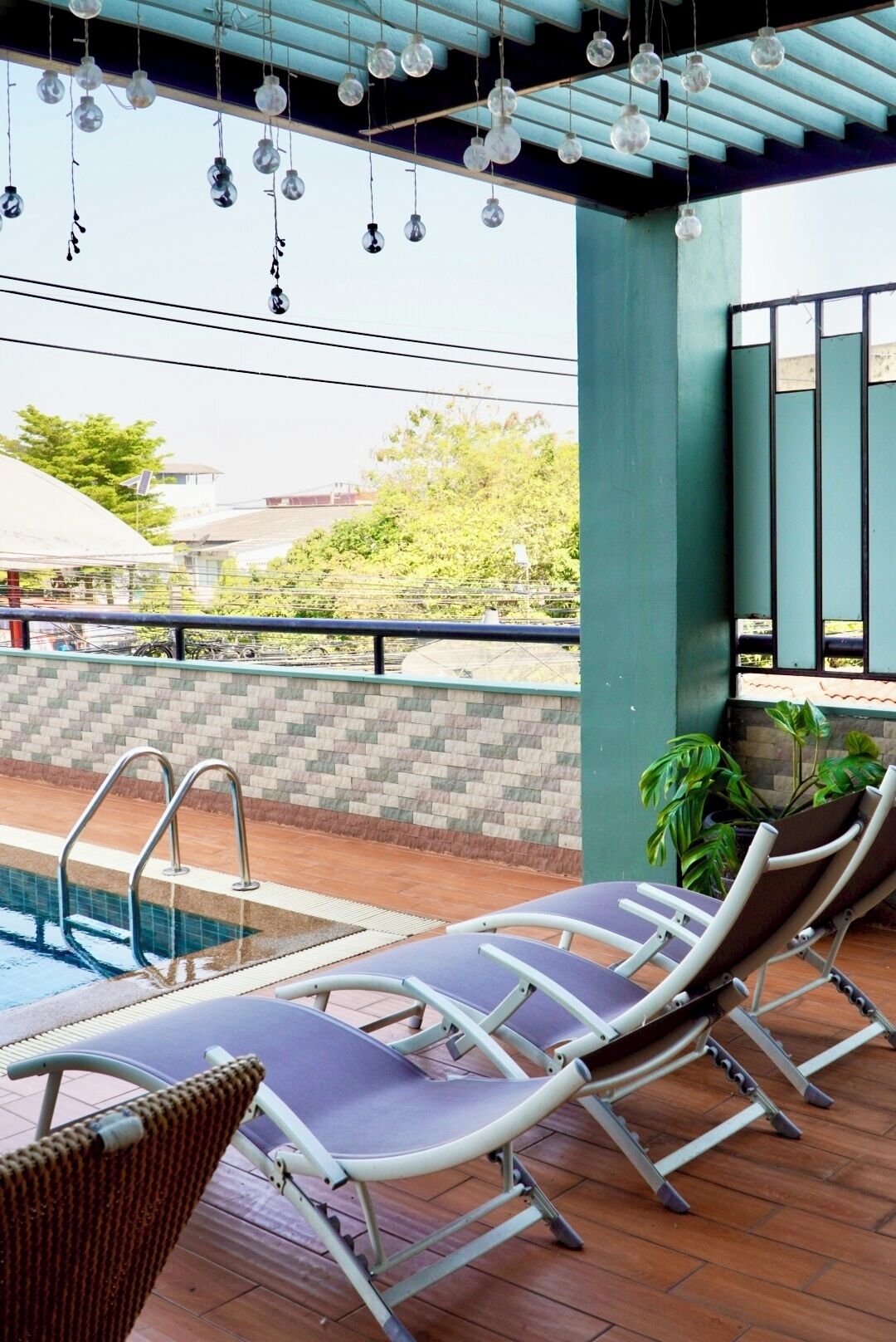 A poolside area with lounge chairs, a tiled floor, and hanging light fixtures.