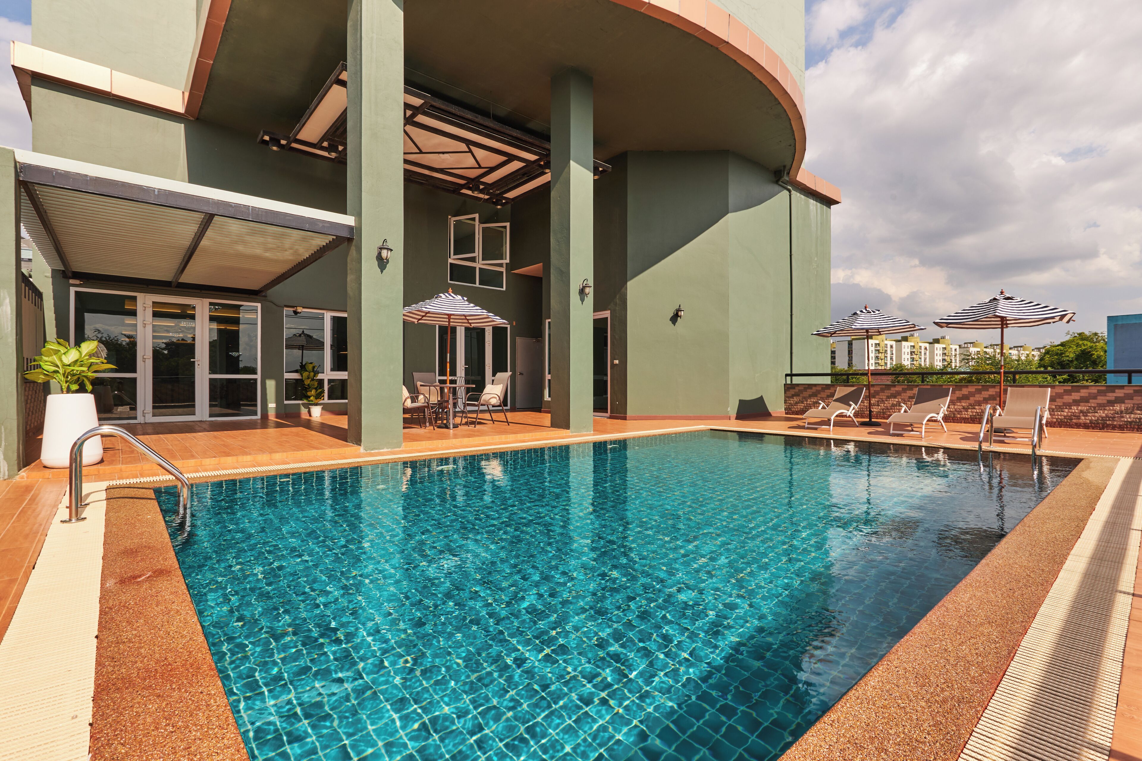 Ein Swimmingpool mit Liegestühlen und Sonnenschirmen, umgeben von einem Gebäude mit einer gewölbten Dachkonstruktion und großen Fenstern.