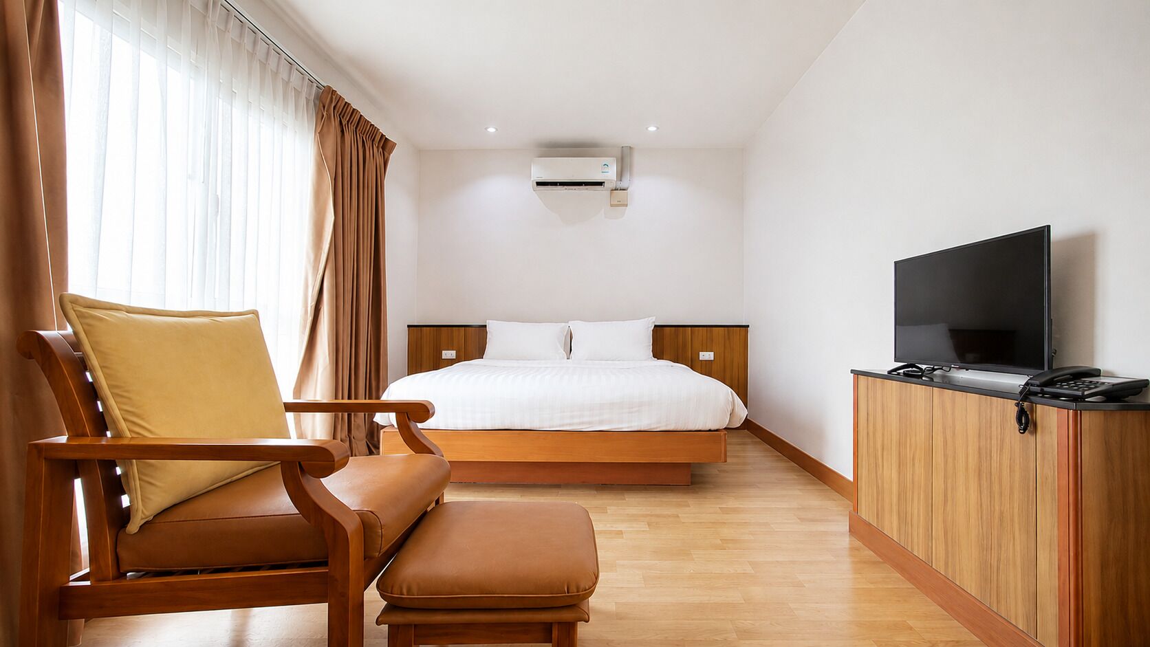 Ein Hotelzimmer mit einem Bett, einem Holzstuhl, einem Fernseher und einer Klimaanlage.