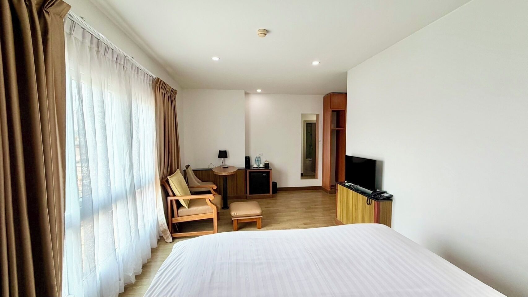 Una habitación de hotel con cama, escritorio con televisor, silla y una mesita.