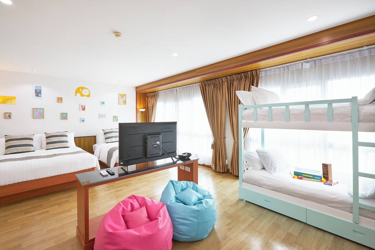A modern hotel room with a bunk bed, a flat-screen TV, a desk with a computer, and bean bags.