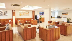 A hotel lobby with wooden seating areas, a reception desk, and a television screen. - Cozy Don Mueang Hotel (Bangkok)