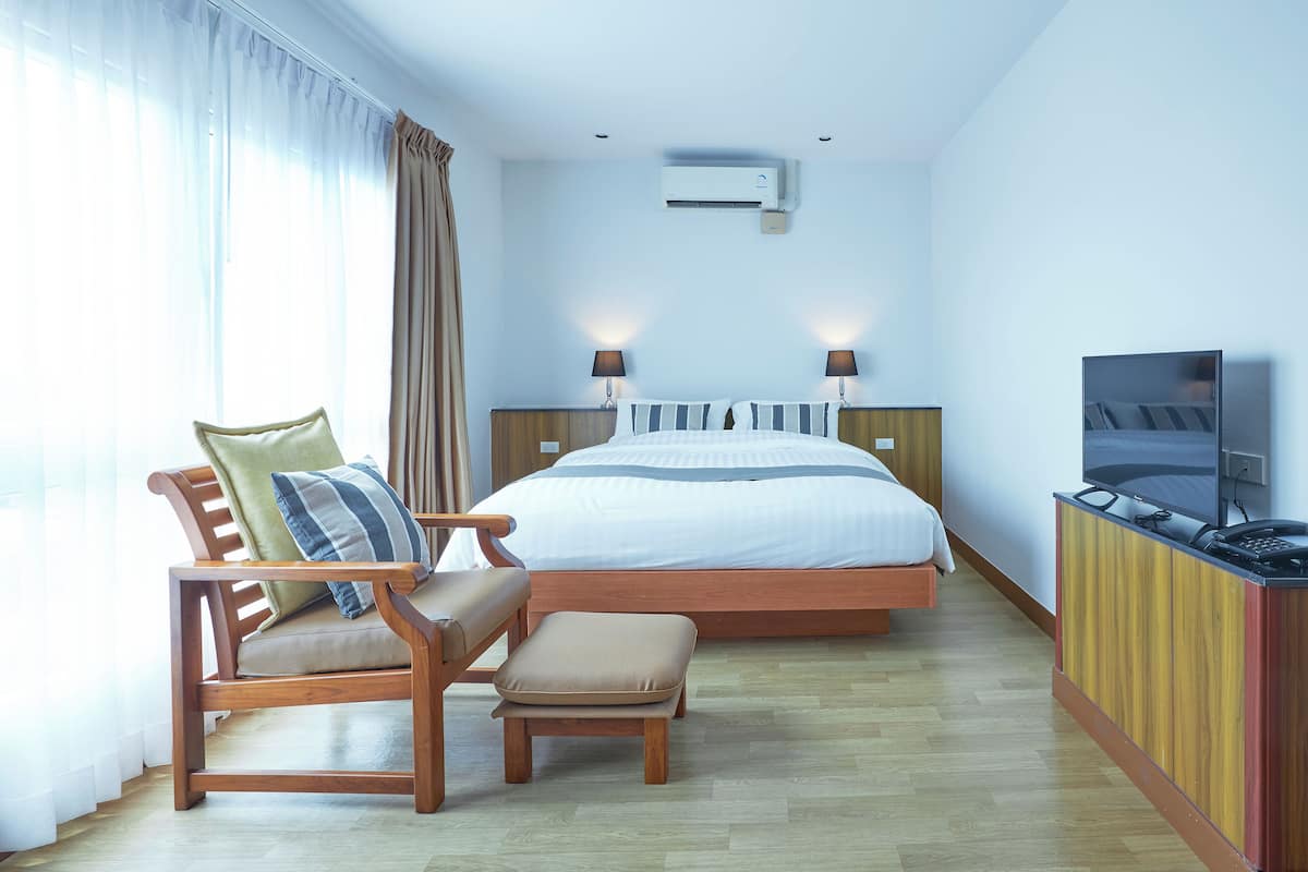 A hotel room with a bed, a wooden chair with a cushion, a small wooden table, and a television on a wooden cabinet.