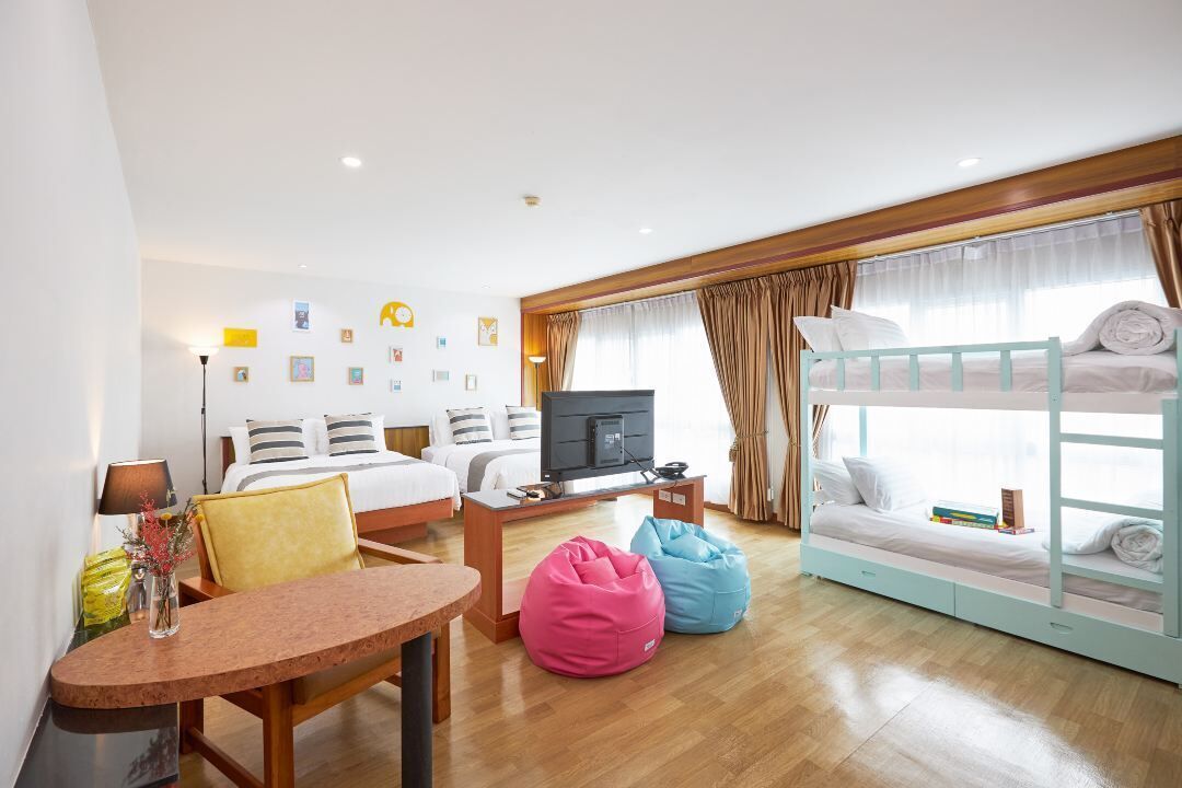 A hotel room with a bunk bed, a television, a desk, and bean bags.