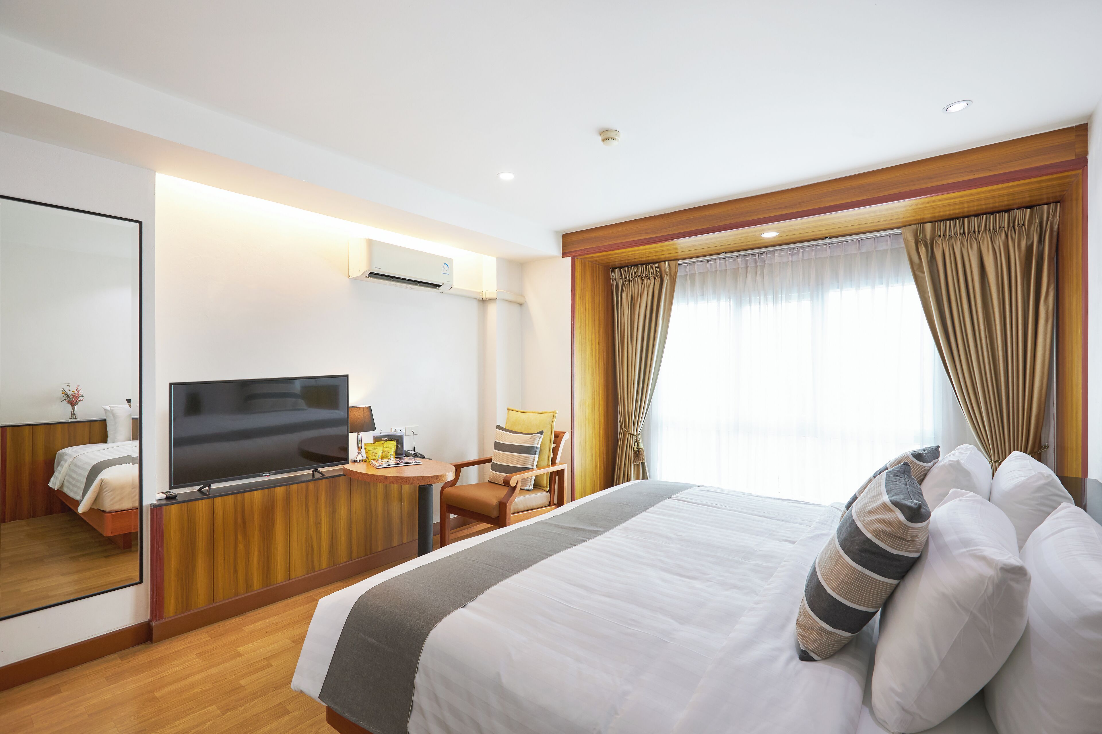 A hotel room with a large bed, a TV, a desk with a chair, and a mirror.