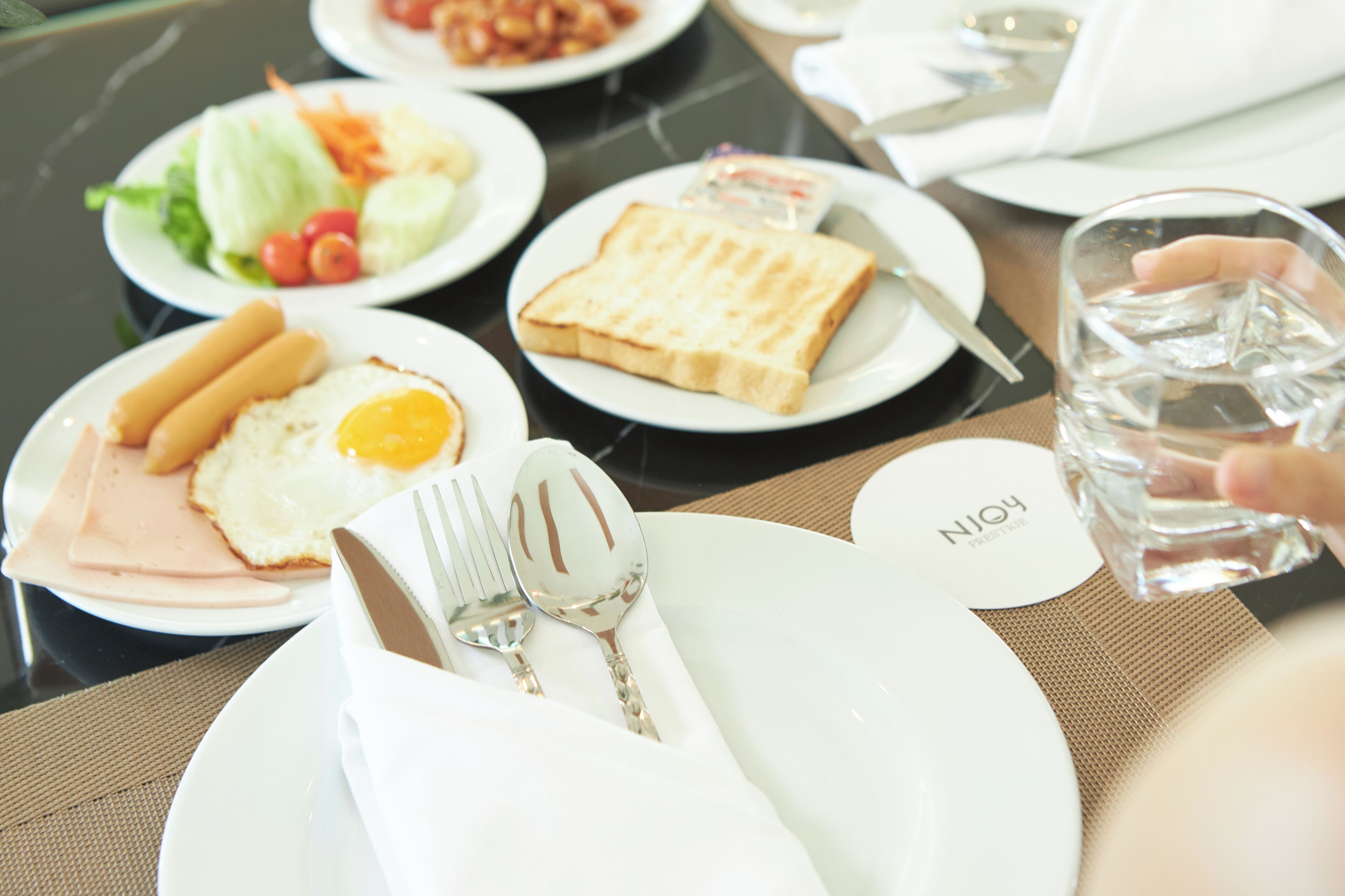Une table mise pour le petit-déjeuner, avec des assiettes remplies de nourriture, des couverts et un verre d’eau.